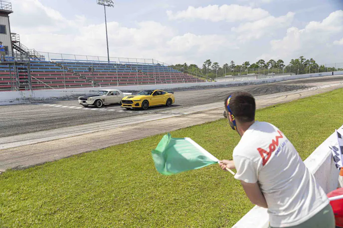 Green flag waving with mustangs on track at start line