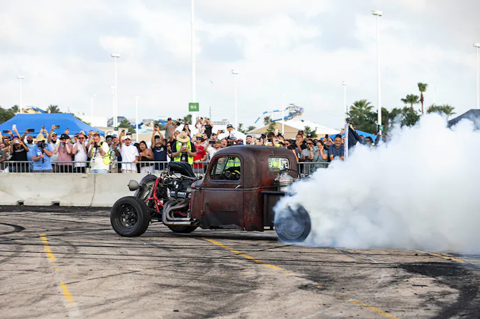 rusty rat rod doing a burnout on pavement with crowd in background